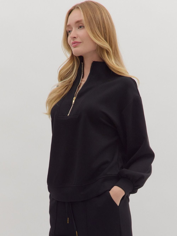 Woman wearing a black zip-up sweatshirt against a plain background