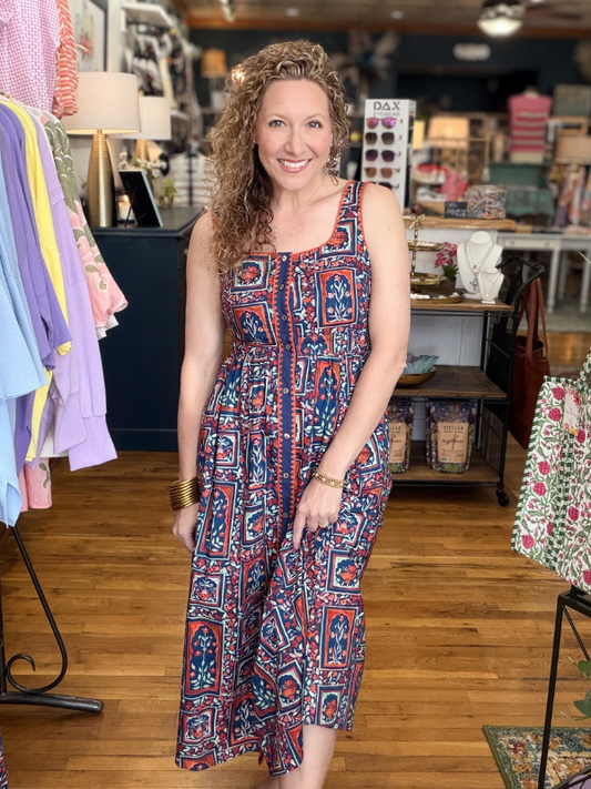 Woman in a patterned dress standing in a store with clothing and shelves in the background