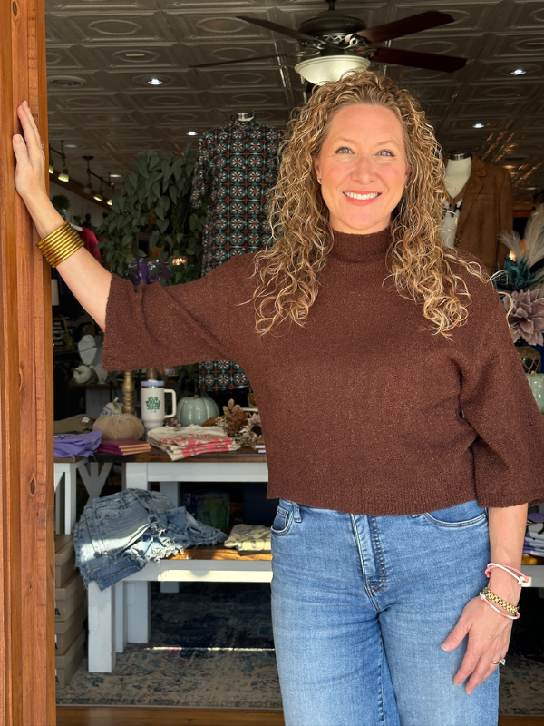 Woman in a brown sweater and blue jeans standing in a store.