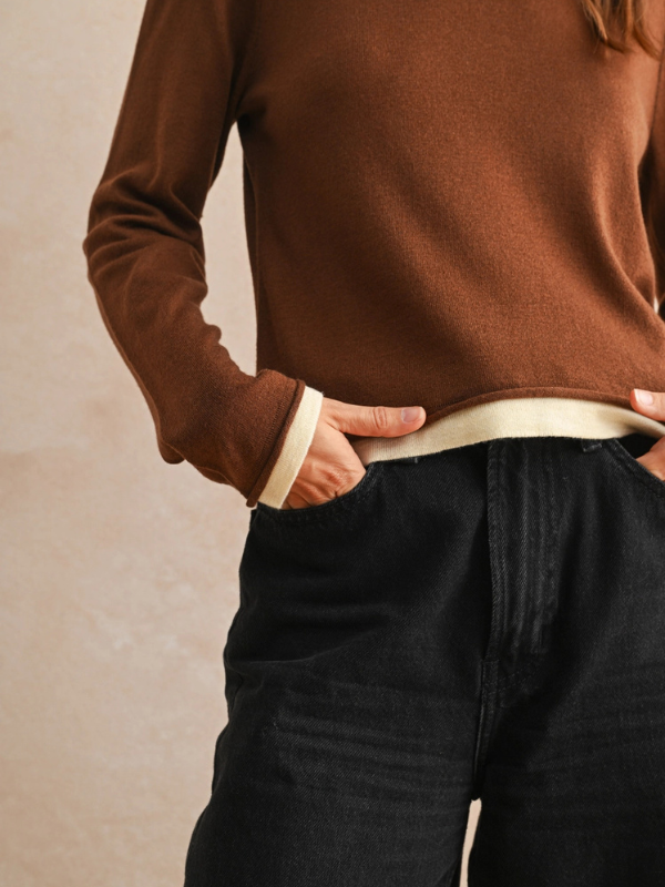 Person wearing a brown sweater and black pants against a beige background