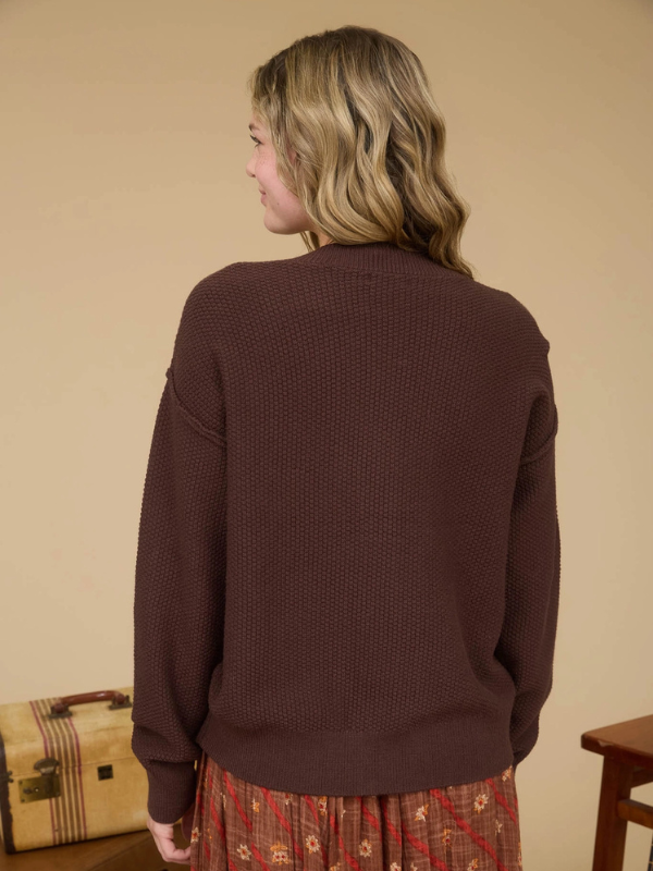 Person wearing a brown sweater with a beige background