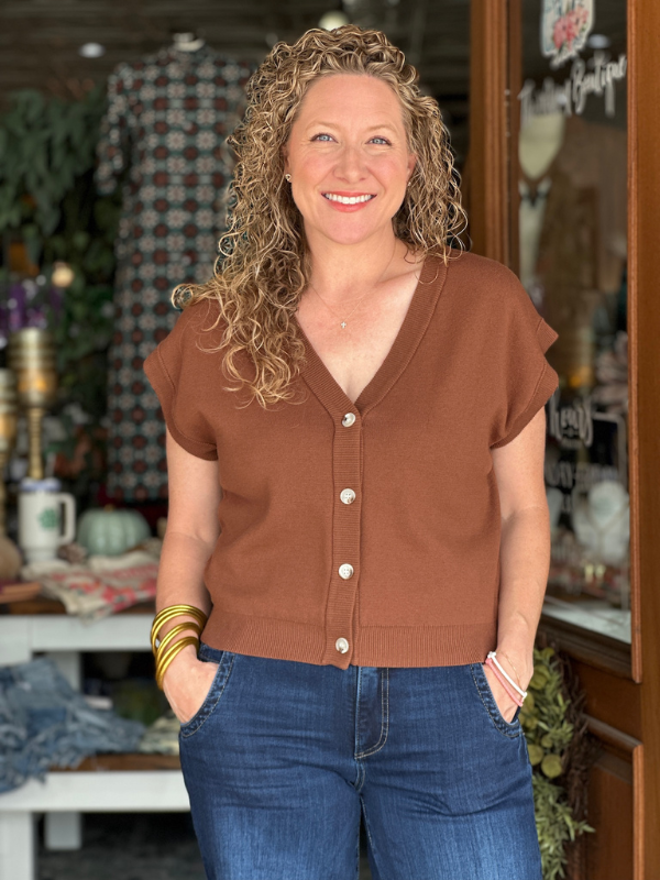 Woman wearing a brown short-sleeve cardigan and blue jeans standing in front of a store.