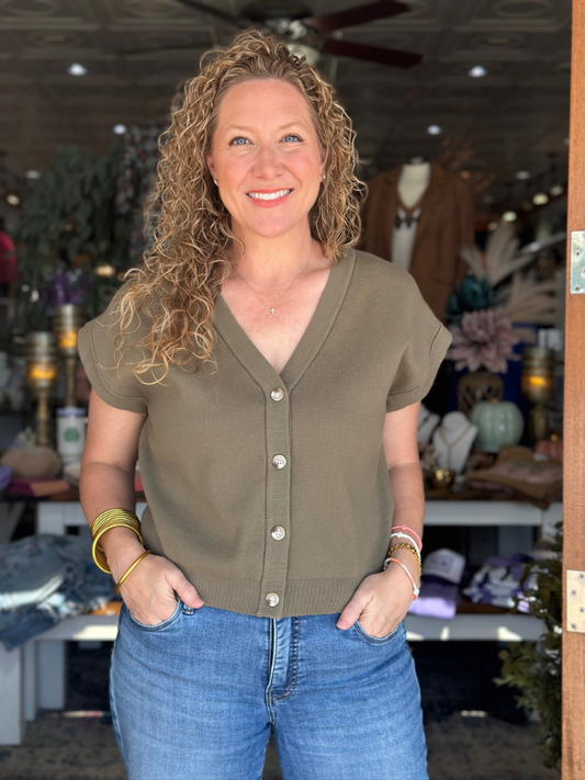 Woman wearing an olive green button-up shirt and blue jeans in a store setting.
