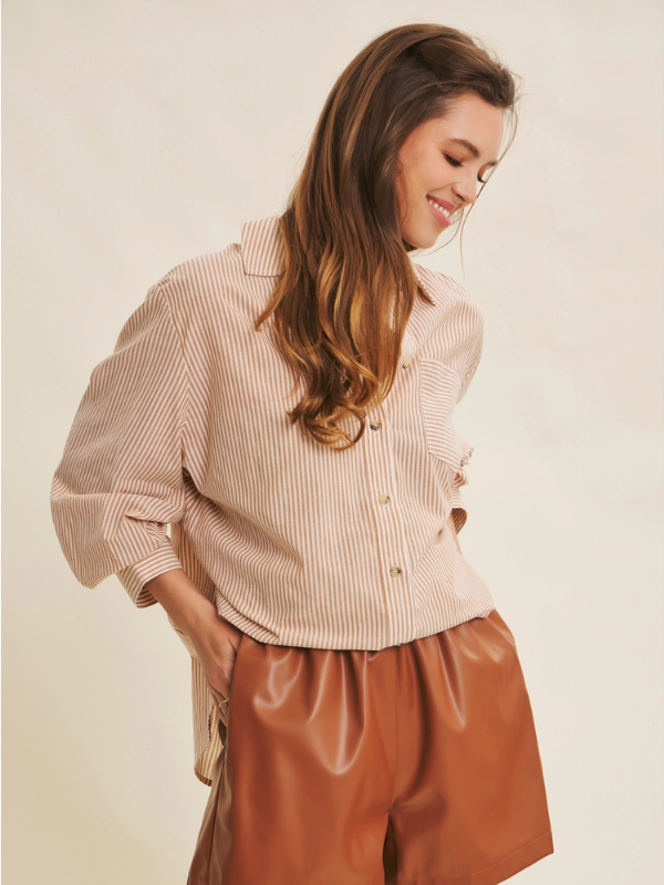 Woman wearing a beige striped shirt and brown shorts on a plain background
