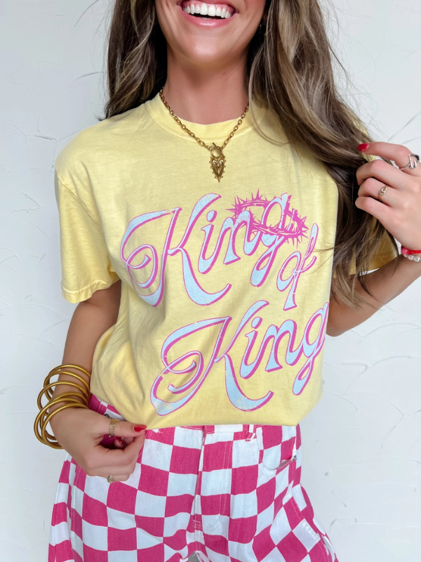 Woman wearing a yellow t-shirt with colorful text and pink checkered pants against a white background