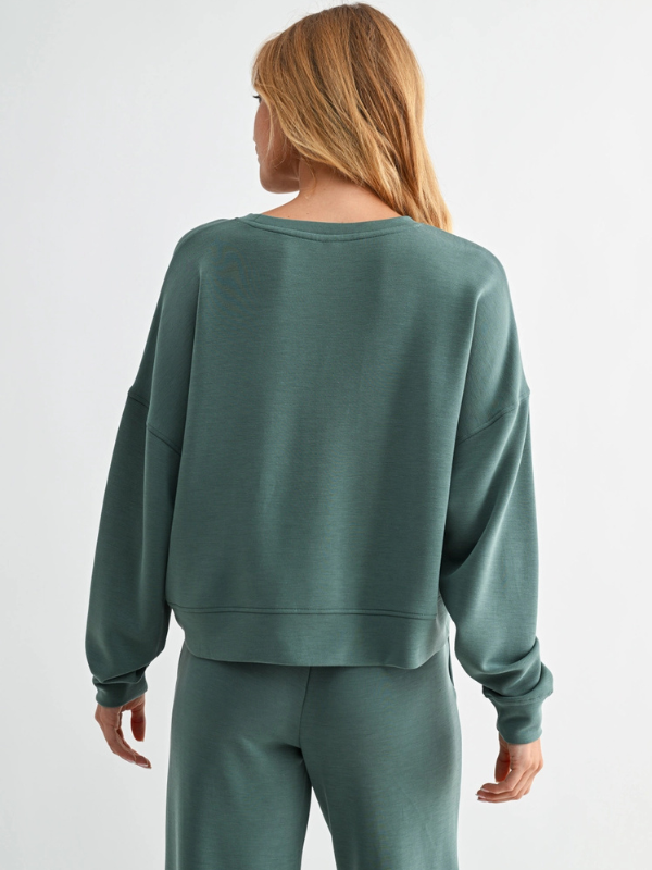 Person wearing a green sweatshirt and pants on a light gray background