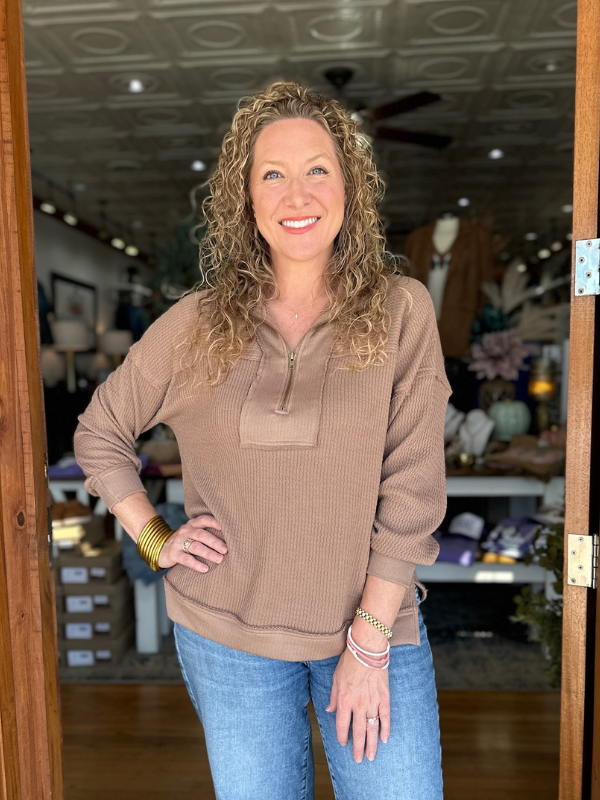 Woman wearing a brown sweater and blue jeans standing in a store.