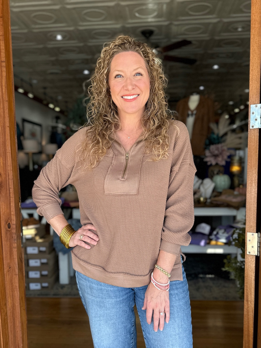 Woman wearing a brown sweater and blue jeans standing in a store.