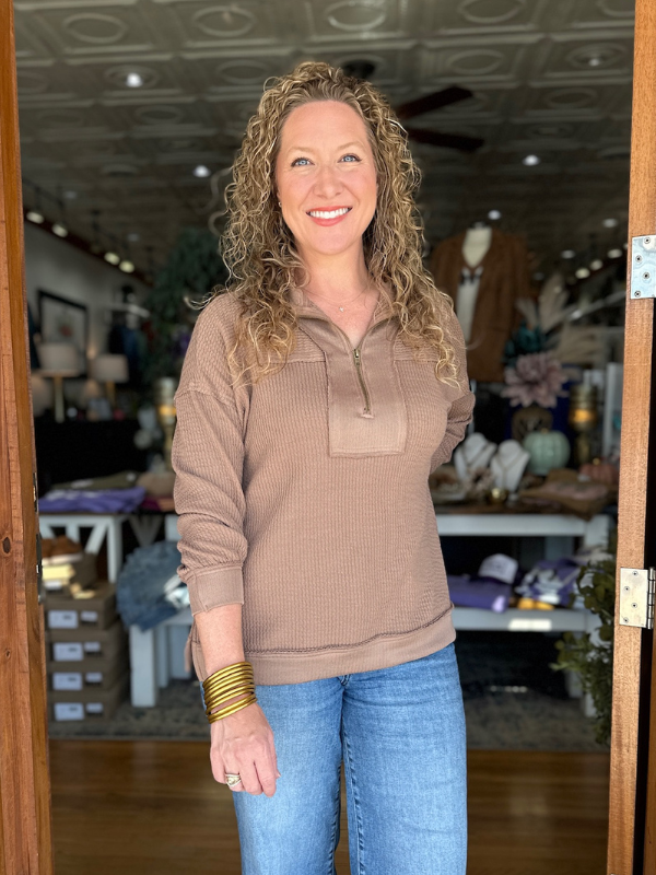Woman wearing a brown sweater and blue jeans standing in a store.