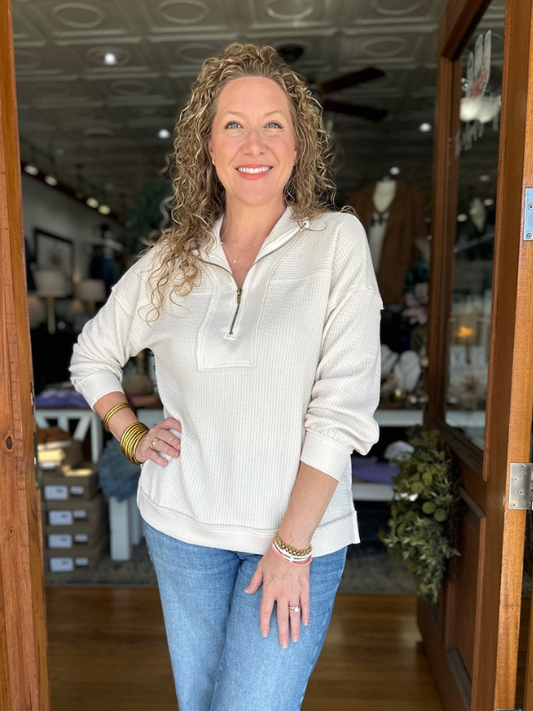 Woman standing in a store doorway wearing a white long-sleeve shirt and blue jeans.