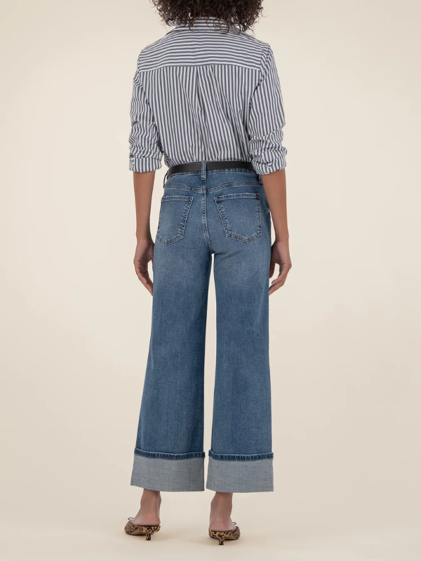 Person wearing a striped shirt and wide-leg jeans on a beige background
