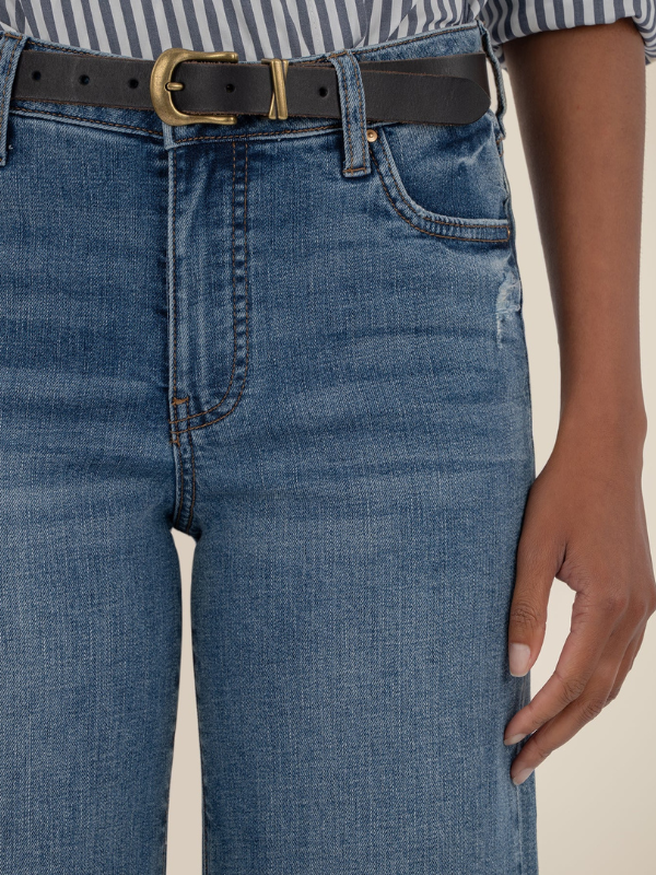 Close-up of blue jeans with a black belt and gold buckle on a neutral background