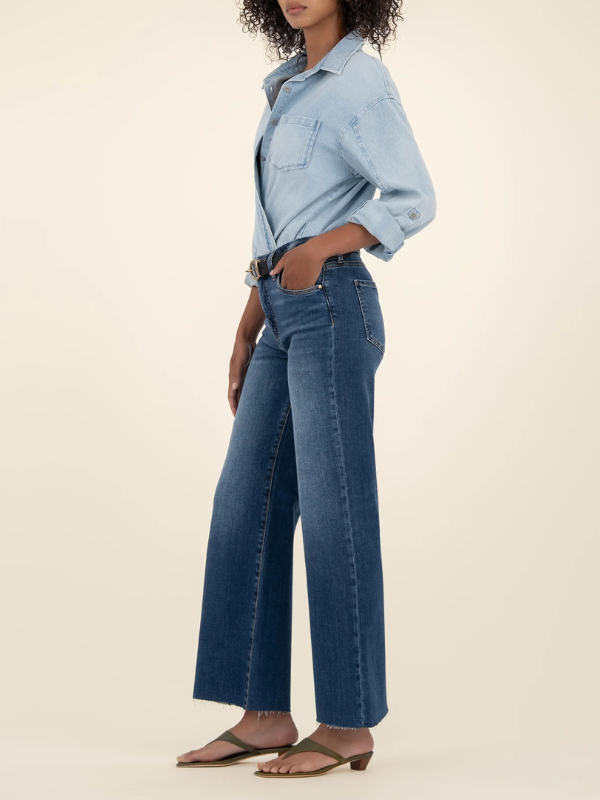 Person wearing a light blue denim shirt and dark blue jeans on a beige background