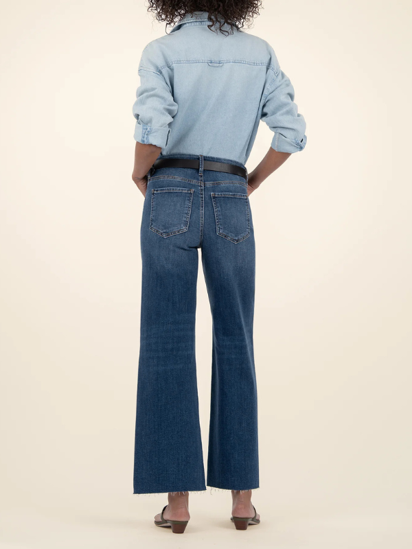 Person wearing a light blue denim shirt and dark blue jeans on a beige background
