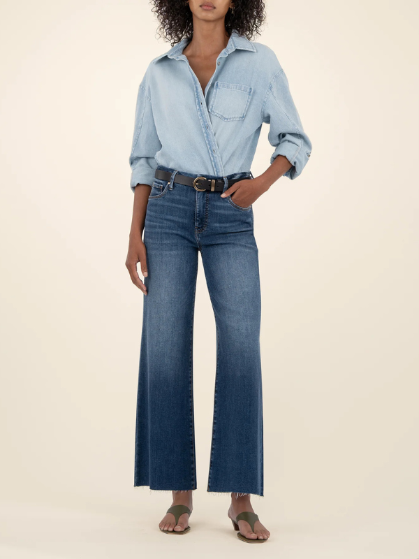 Person wearing a light blue denim shirt and dark blue jeans on a beige background