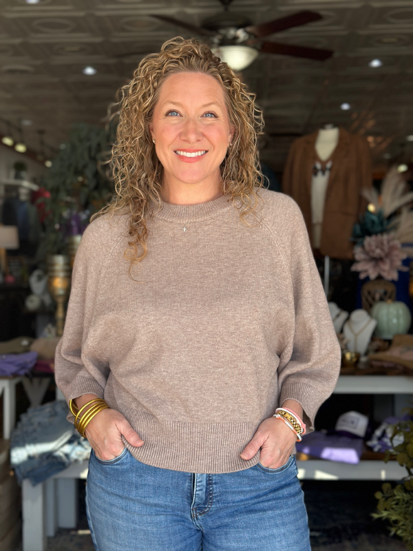 Woman wearing a beige sweater and blue jeans in a store setting