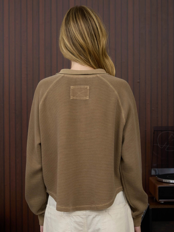 Person wearing a brown sweater with a visible brand logo against a wooden panel background