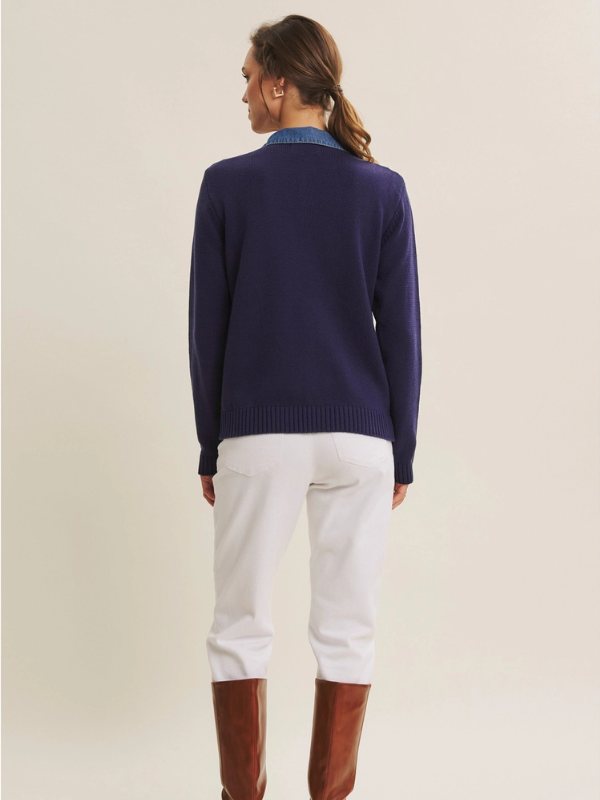 Person wearing a navy sweater and white pants on a beige background