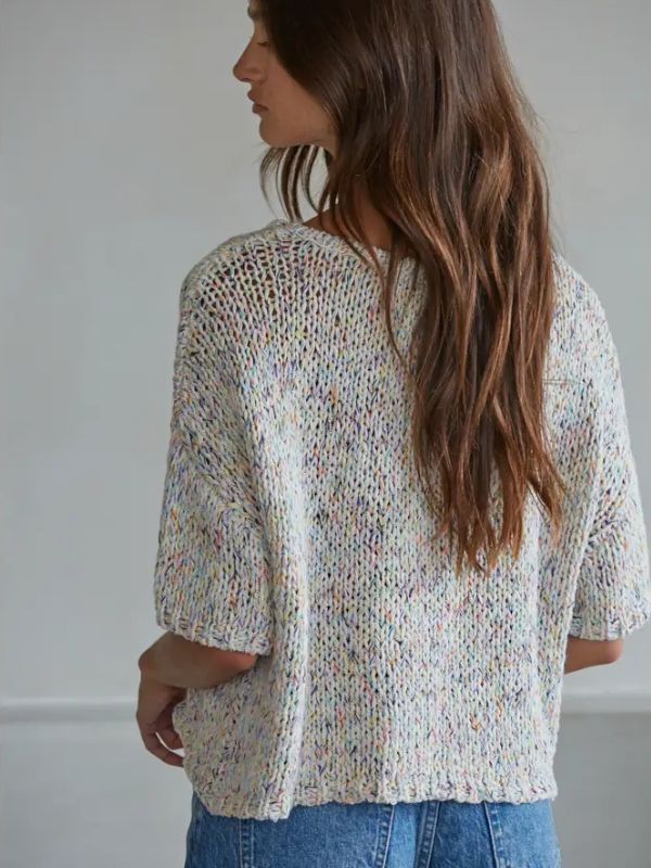 Woman wearing a textured, multicolored sweater against a plain background