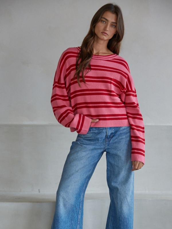Woman wearing a pink and red striped sweater and blue jeans against a plain background