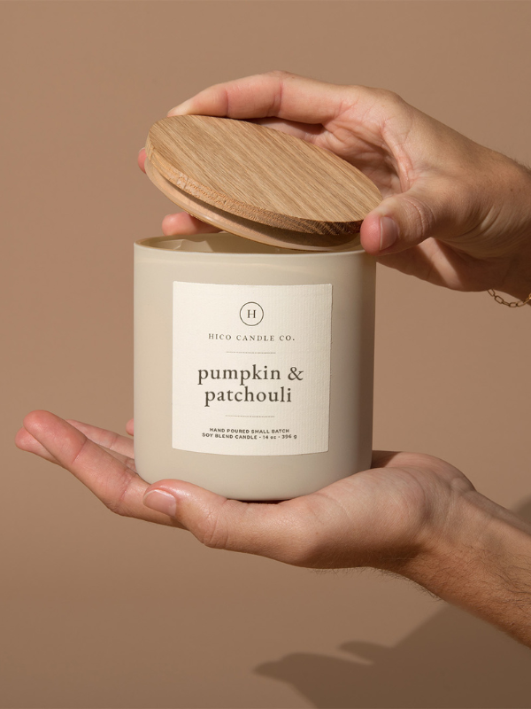 Hand holding a candle labeled 'pumpkin & patchouli' by High Candle Co. on a beige background