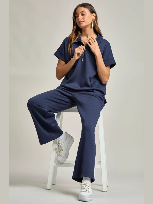 Woman wearing a navy blue outfit sitting on a white stool against a light gray background