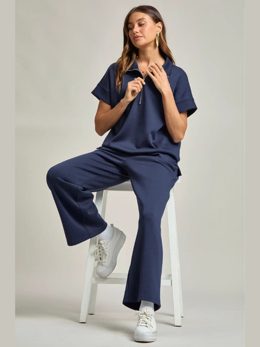 Woman wearing a navy blue outfit sitting on a white stool against a light gray background