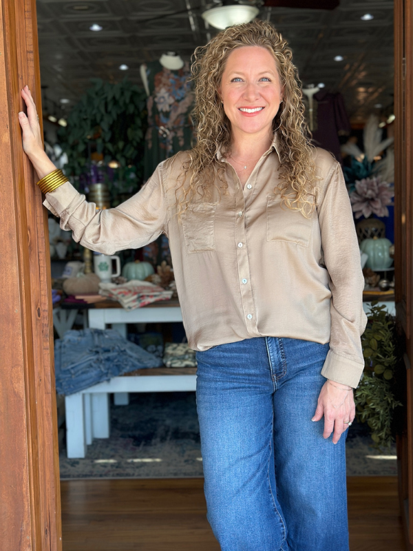 Woman standing in a store doorway wearing a beige shirt and blue jeans.