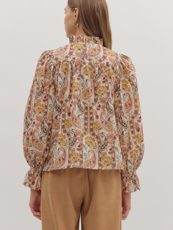 Person wearing a patterned blouse with long sleeves on a plain background