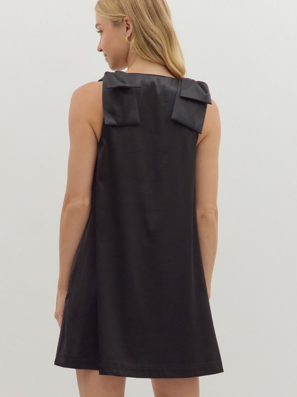 Black sleeveless dress with large bow detail on the back, worn by a model against a plain background.
