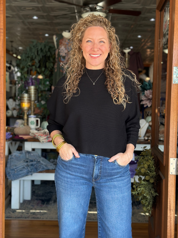 Woman wearing a black top and blue jeans standing in a store.