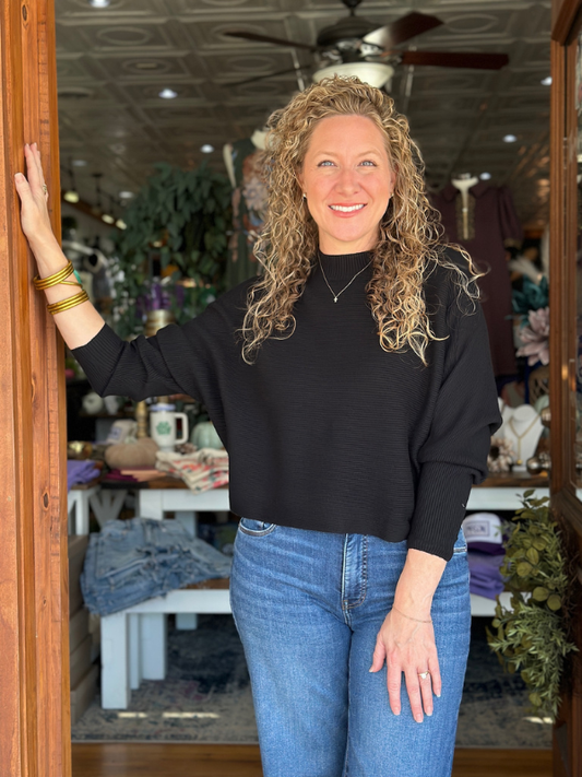 Woman standing in a store doorway wearing a black sweater and blue jeans.