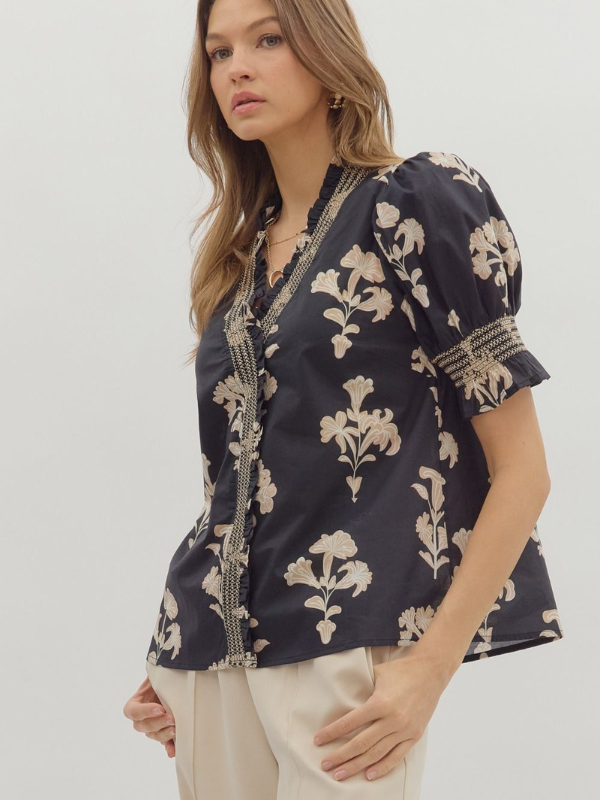 Woman wearing a navy blue blouse with beige floral patterns on a white background