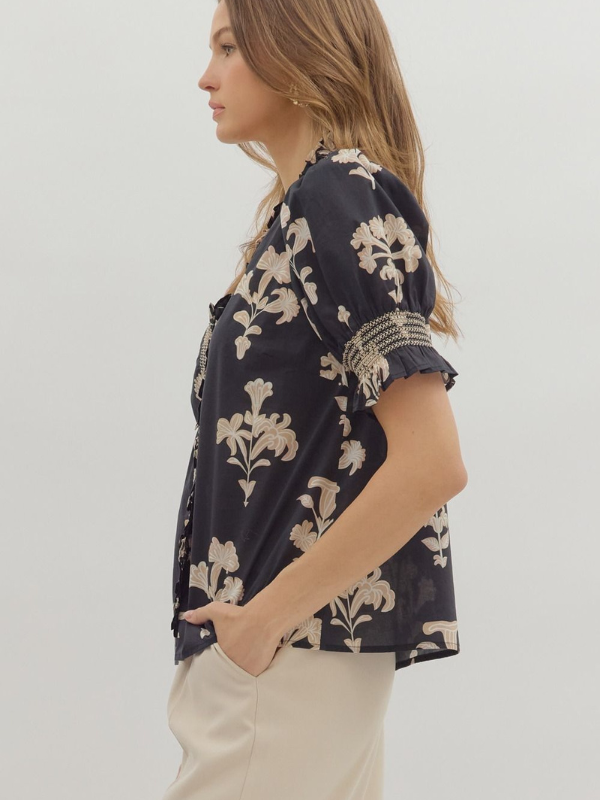 Woman wearing a black floral blouse with beige accents on a white background