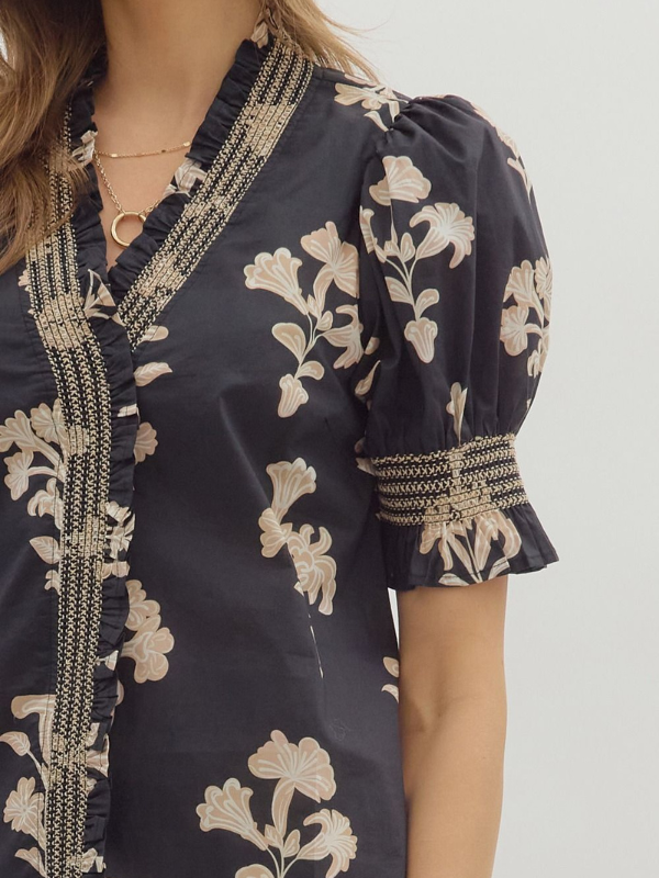 Navy blue blouse with beige floral patterns and ruffled details on a plain background