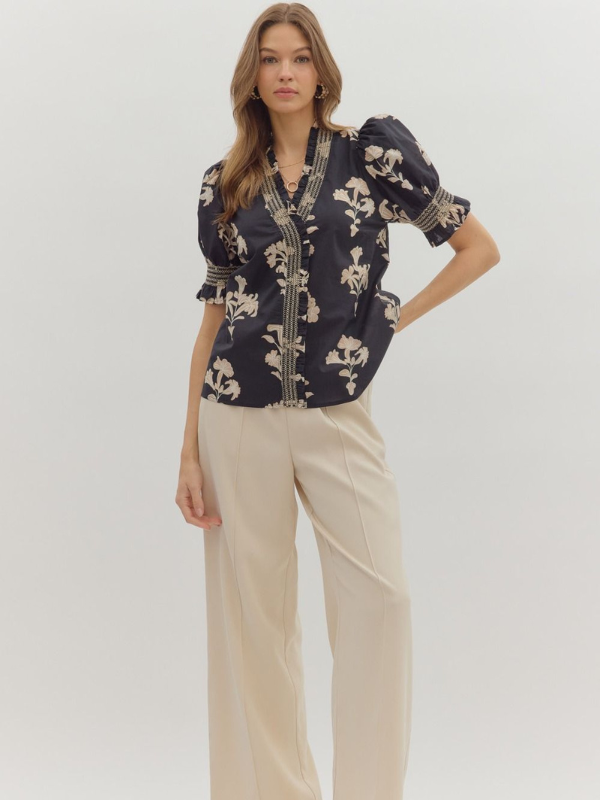 Woman wearing a navy floral blouse and beige pants on a white background