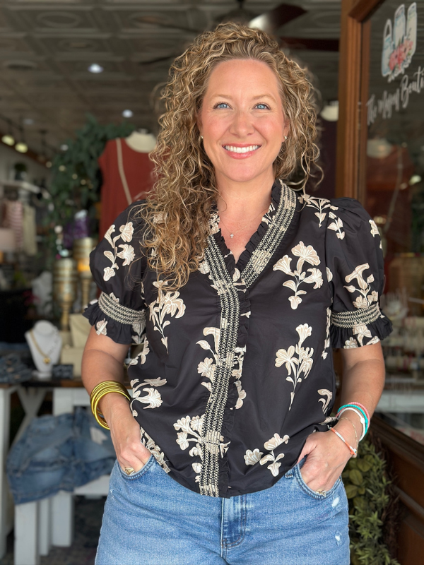 Woman wearing a black floral blouse and blue jeans in an indoor setting
