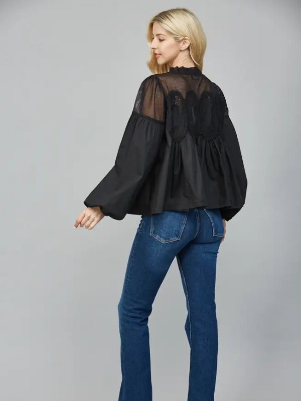 Woman wearing a black blouse with sheer panels and blue jeans on a gray background