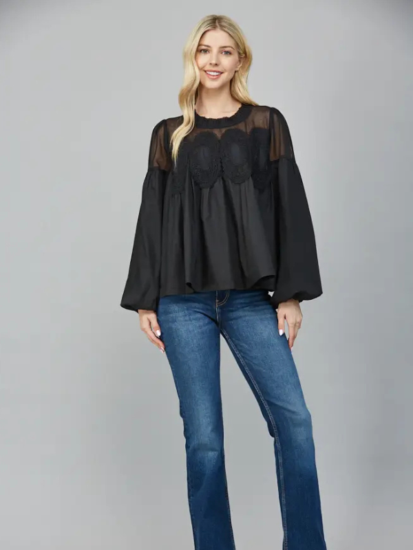 Woman wearing a black blouse with sheer panels and blue jeans on a gray background