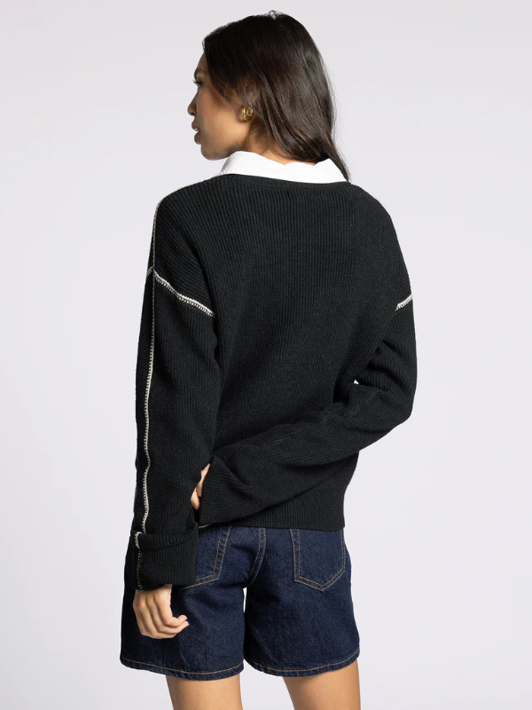 Person wearing a black sweater with white trim on a plain background