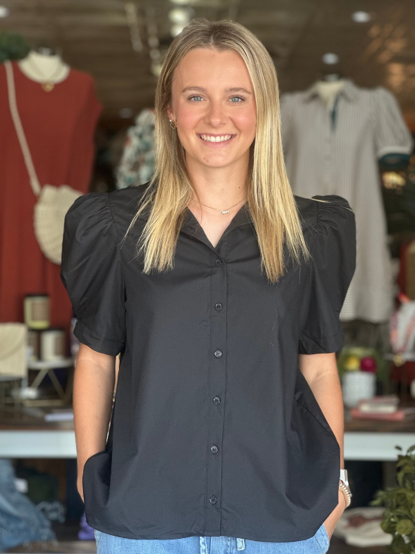 Woman wearing a black blouse with puff sleeves in a clothing store.