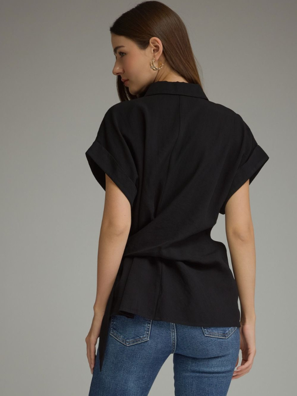 A woman shown from the back wearing a black short-sleeve wrap-style blouse and blue jeans against a plain gray studio background.