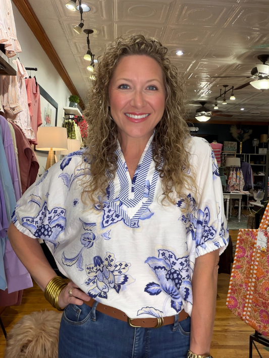 Woman wearing a white blouse with blue floral patterns in a clothing store.