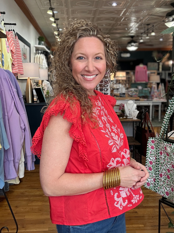 Woman in a red top with white floral patterns standing in a store.