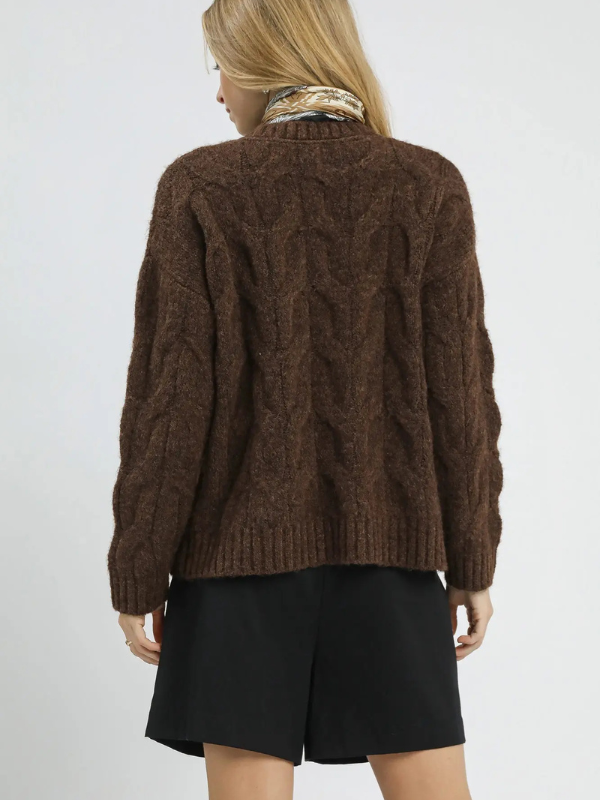Person wearing a brown cable knit sweater and black shorts on a white background