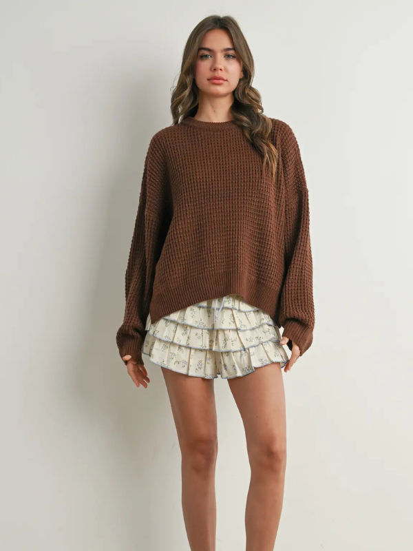 Woman wearing a brown sweater and patterned skirt on a plain background