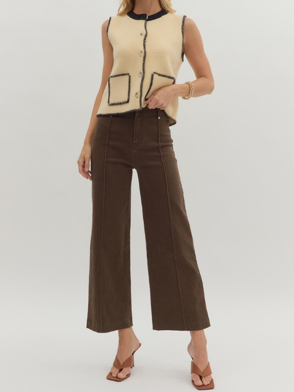 Person wearing a beige sleeveless vest with black accents and brown wide-leg pants on a white background