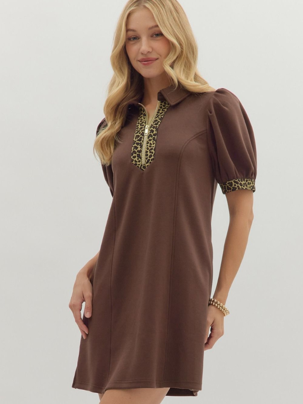 Woman wearing a brown dress with leopard print accents on a plain background