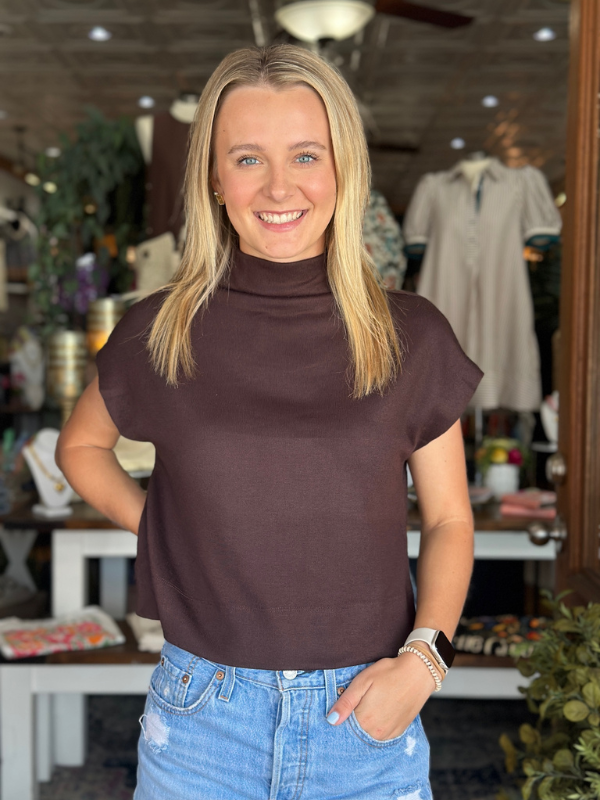 Woman wearing a brown turtleneck top and blue jeans in a store setting