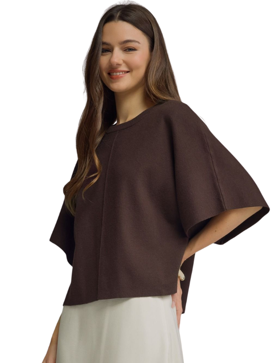 A woman modeling a dark brown cape-sleeve top with a round neckline, paired with a light-colored skirt, against a plain white background.